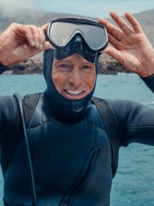 man in scuba gear, raises goggles, and smiles