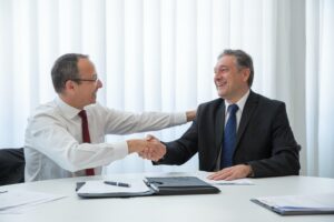 seated at a table, a pleased business owner shaking hands with his insurance agent